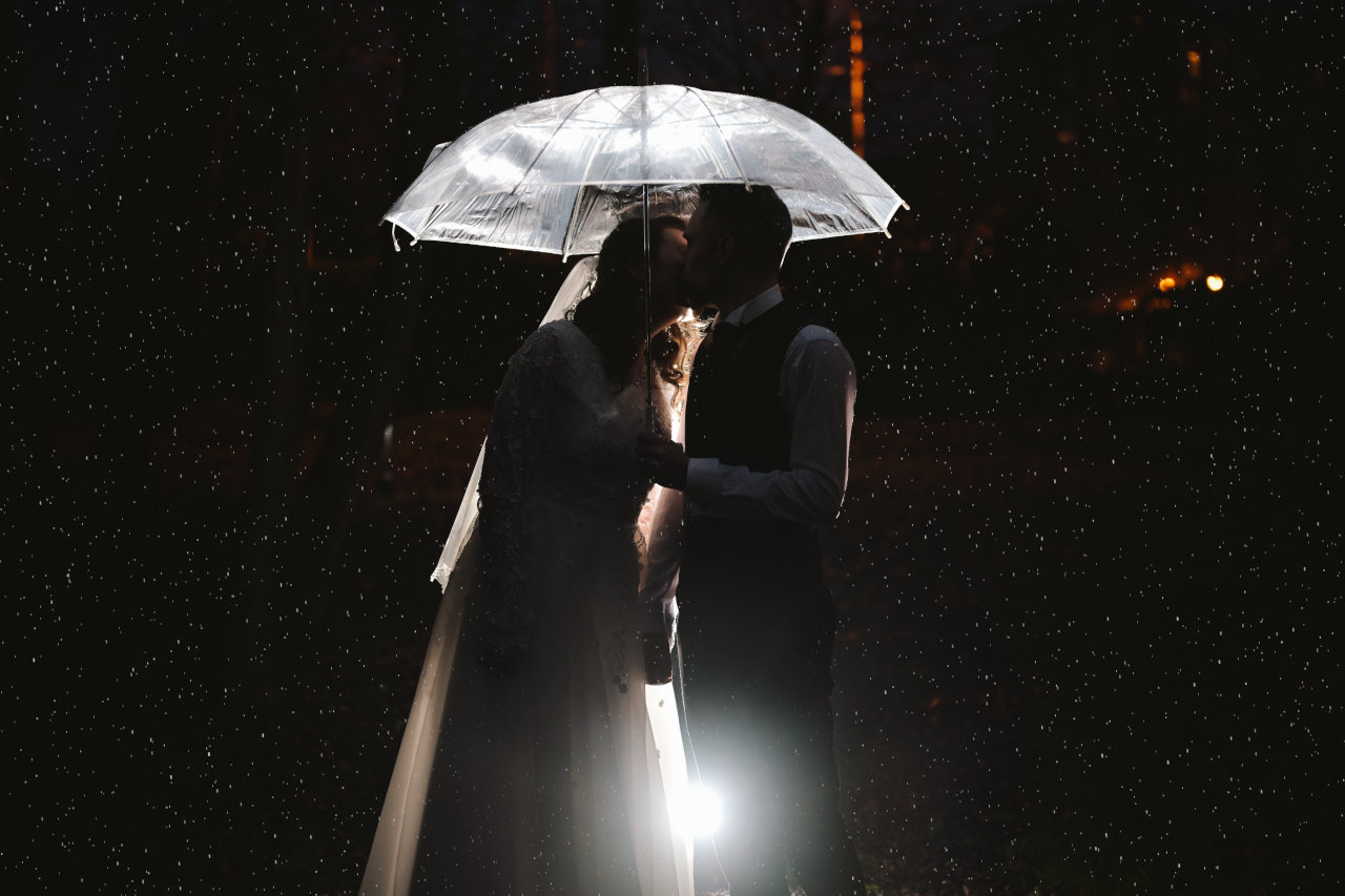 Tečaj fotografiranja vjenčanja – mladenci pod kišobranom, fotografirani na kiši korištenjem off camera flash tehnike.
